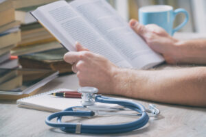 Young doctor is learning and preparing for the exam, he is using books and tablet to search for knowledge
